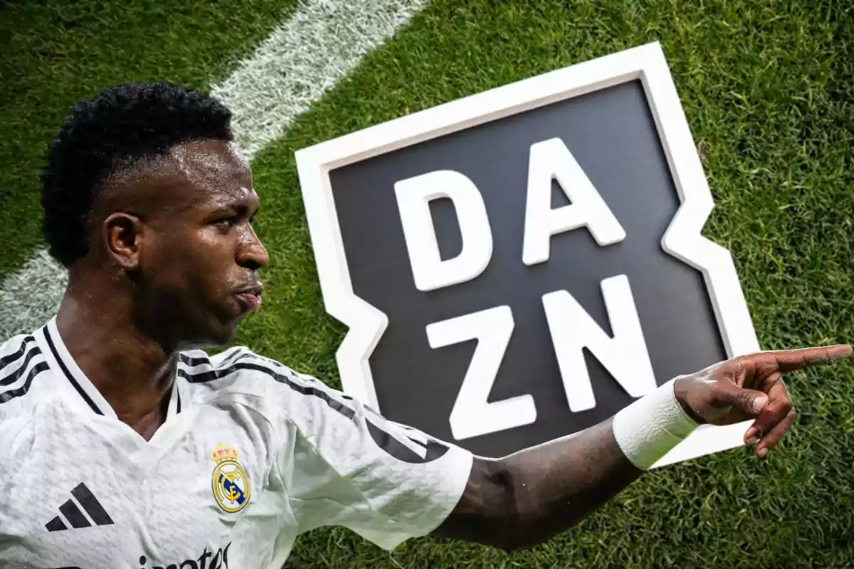 Jugador de fútbol con uniforme blanco señalando hacia la derecha con un cartel de DAZN en el fondo sobre el césped.