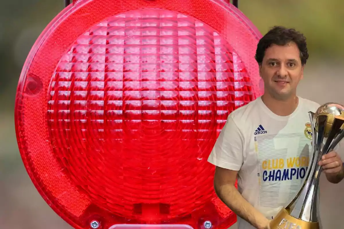 Un hombre con una camiseta de fútbol del Real Madrid sostiene un trofeo frente a una luz roja grande.