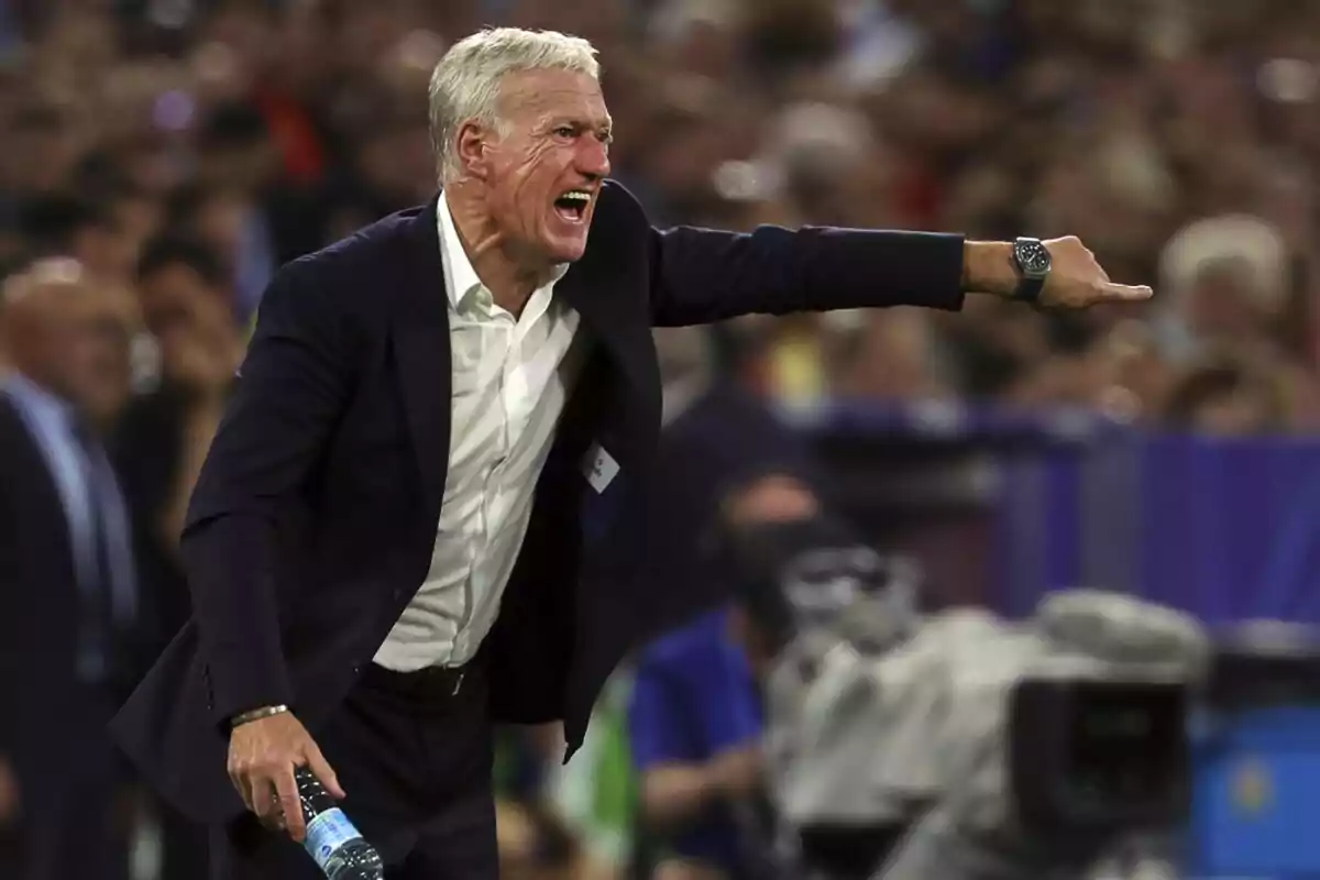 Un hombre de cabello canoso, vestido con traje oscuro y camisa blanca, grita y señala con el brazo extendido durante un evento deportivo. Un hombre de cabello canoso, vestido con traje oscuro y camisa blanca, grita y señala con el brazo extendido durante un evento deportivo.