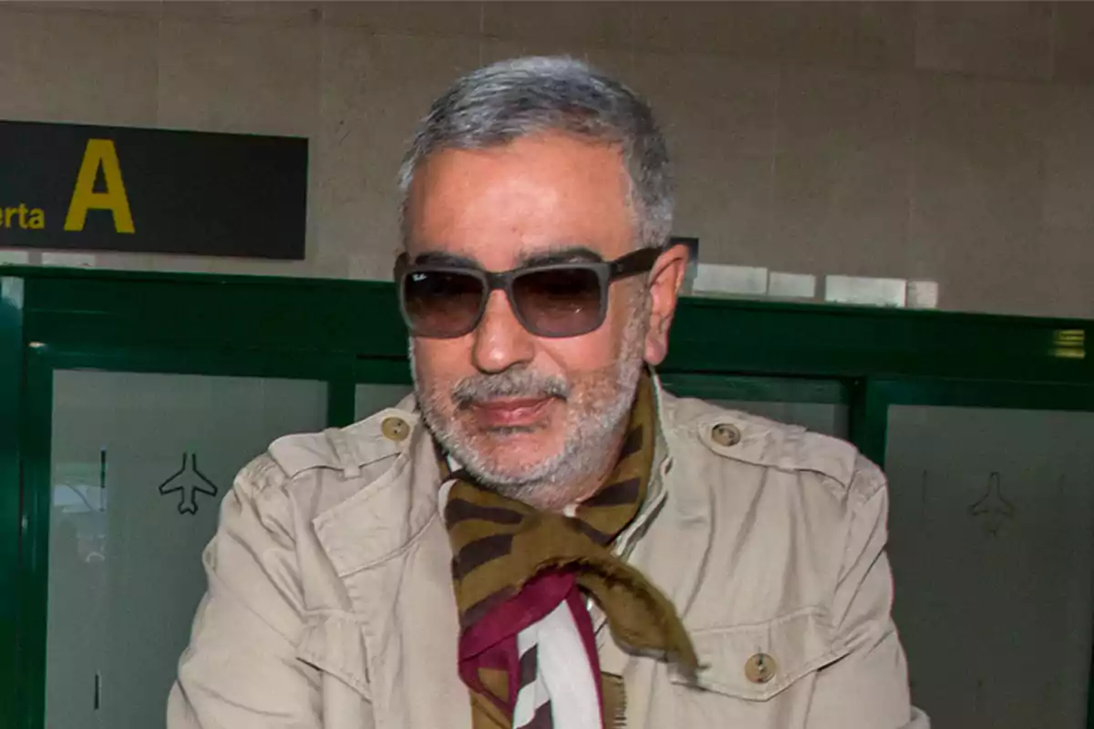 Hombre con gafas de sol y bufanda en un entorno de aeropuerto.