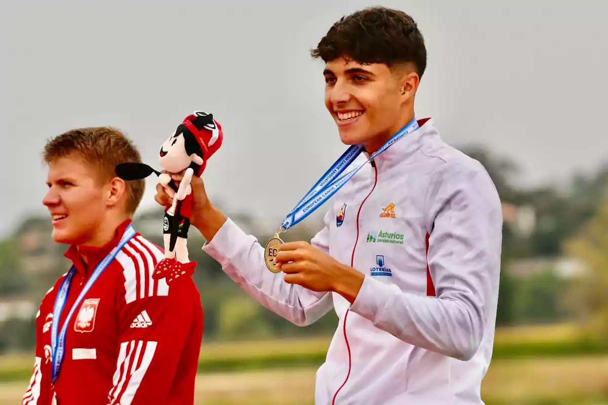 Dos atletas en el podio, uno de ellos sosteniendo una medalla y un peluche.