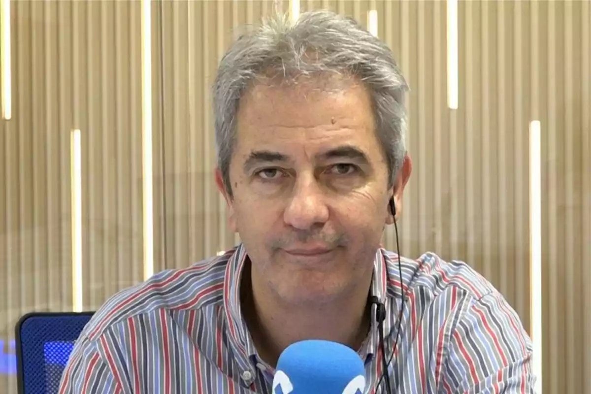 Hombre de cabello canoso con camisa a rayas frente a un micrófono azul en un estudio de grabación. Hombre de cabello canoso con camisa a rayas frente a un micrófono azul en un estudio de grabación.