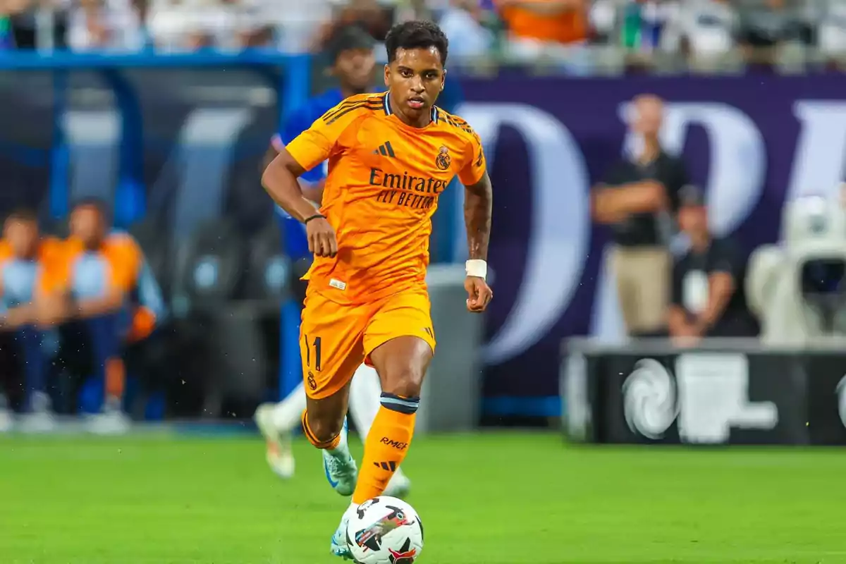 Un jugador de fútbol con el uniforme naranja del Real Madrid corre con el balón en el campo durante un partido.