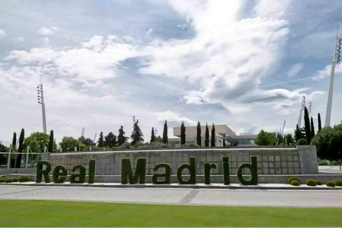 Entrada al complejo deportivo del Real Madrid con letras verdes y un cielo parcialmente nublado. Entrada al complejo deportivo del Real Madrid con letras verdes y un cielo parcialmente nublado.