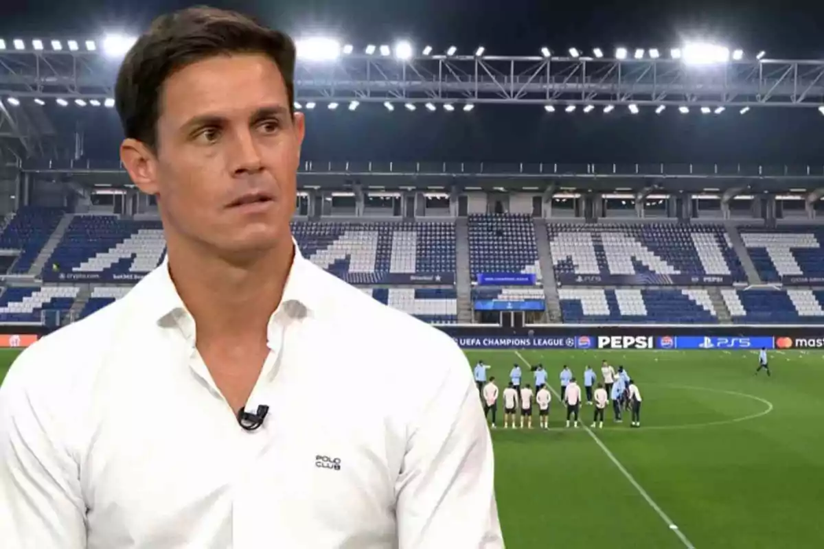 Un hombre con camisa blanca está en primer plano mientras al fondo se ve un estadio de fútbol iluminado y un grupo de jugadores en el campo.