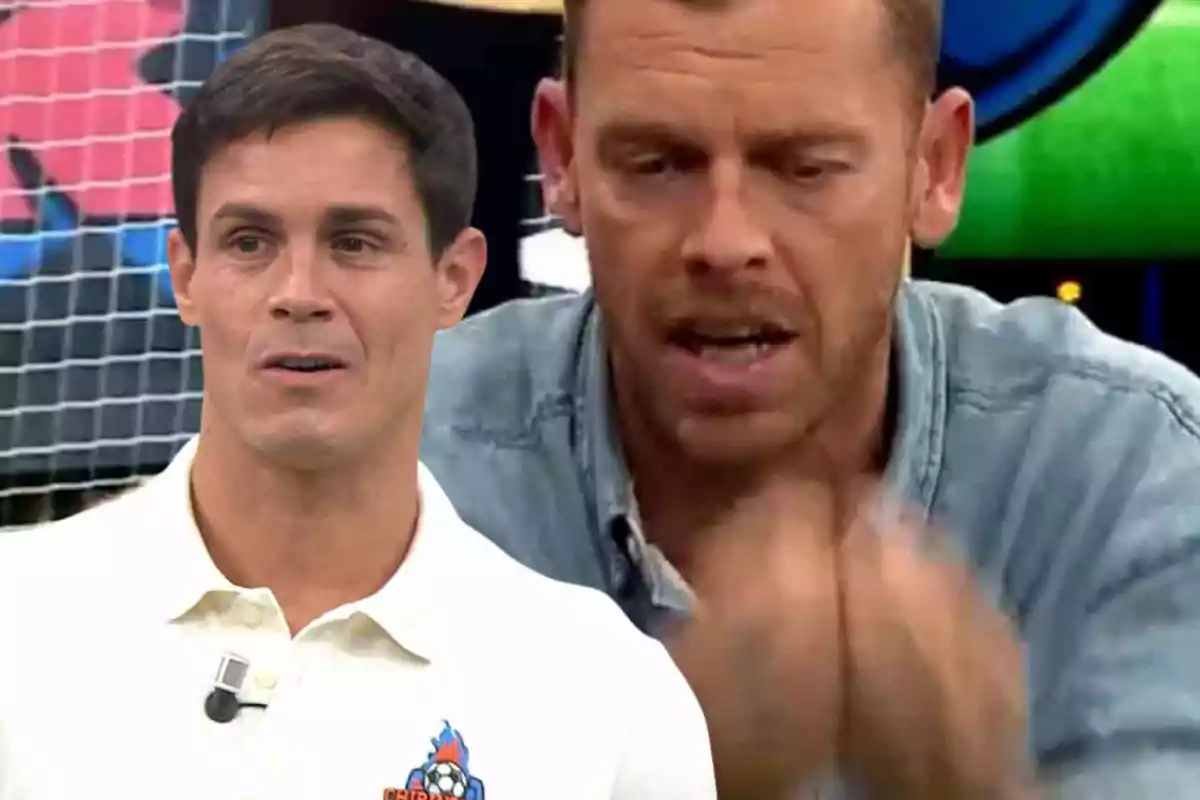 Dos hombres en un programa de televisión, uno con camisa blanca y el otro con chaqueta de mezclilla, en un entorno colorido.