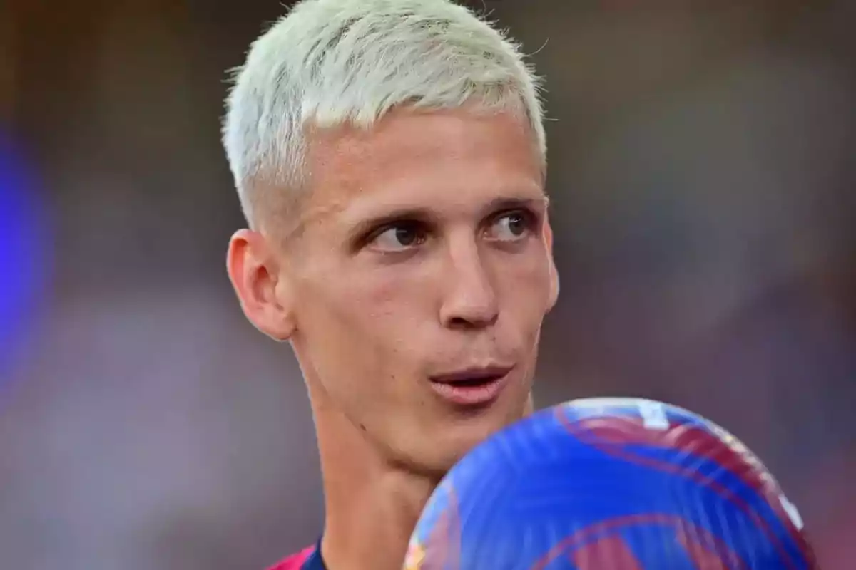 Un hombre con cabello rubio platinado sosteniendo un balón de fútbol.