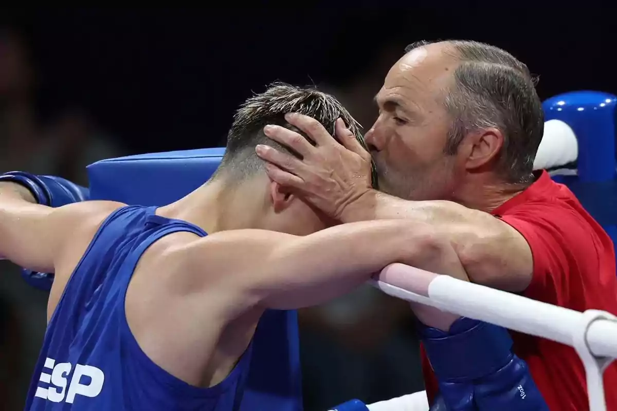 Entrenador besa la cabeza de un boxeador en el ring mientras lo consuela.