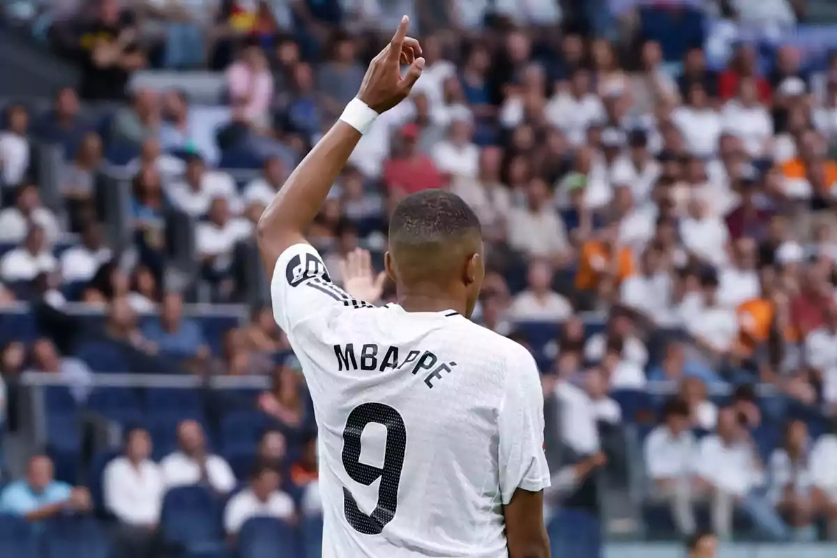 Jugador de fútbol con la camiseta número 9 levantando un brazo en un estadio lleno de espectadores.