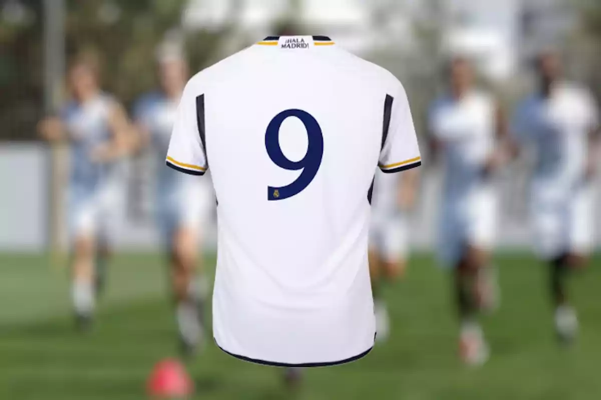 Camiseta de fútbol blanca con el número 9 en la espalda y la inscripción "Hala Madrid" en el cuello, con jugadores desenfocados al fondo.