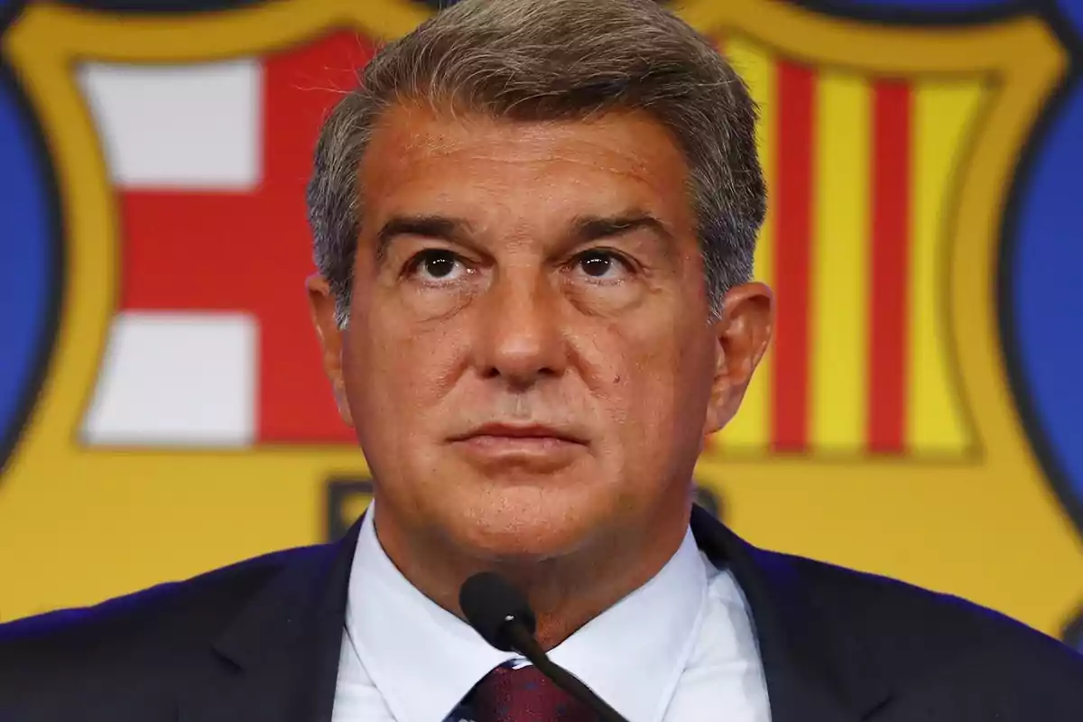 Hombre de traje y corbata hablando en una conferencia de prensa con el escudo del FC Barcelona de fondo.