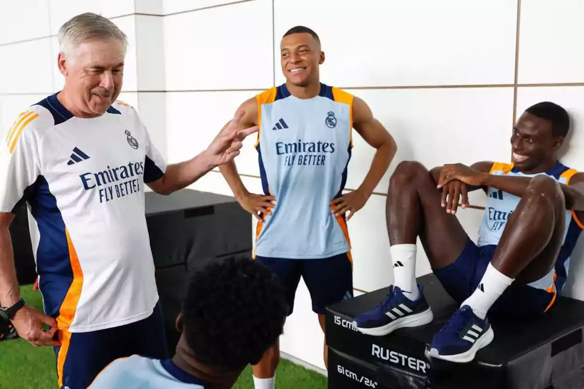 Un grupo de personas con ropa deportiva del Real Madrid conversando y sonriendo en un ambiente interior.