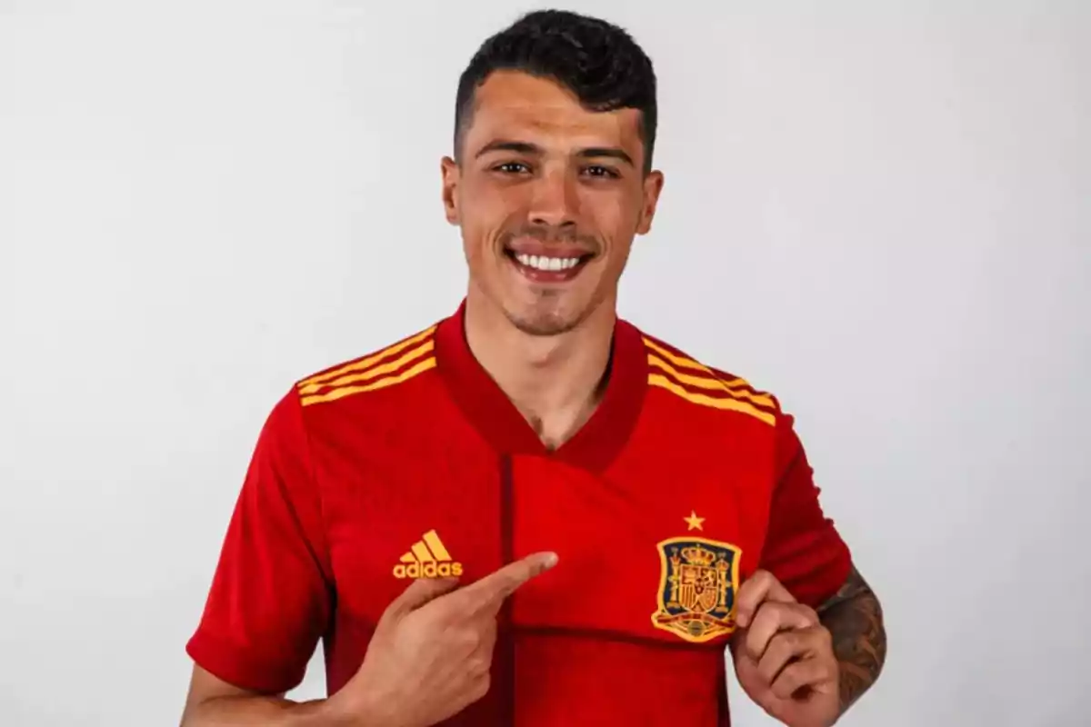 Hombre sonriendo con la camiseta roja de la selección de fútbol de España señalando el escudo. Hombre sonriendo con la camiseta roja de la selección de fútbol de España señalando el escudo.