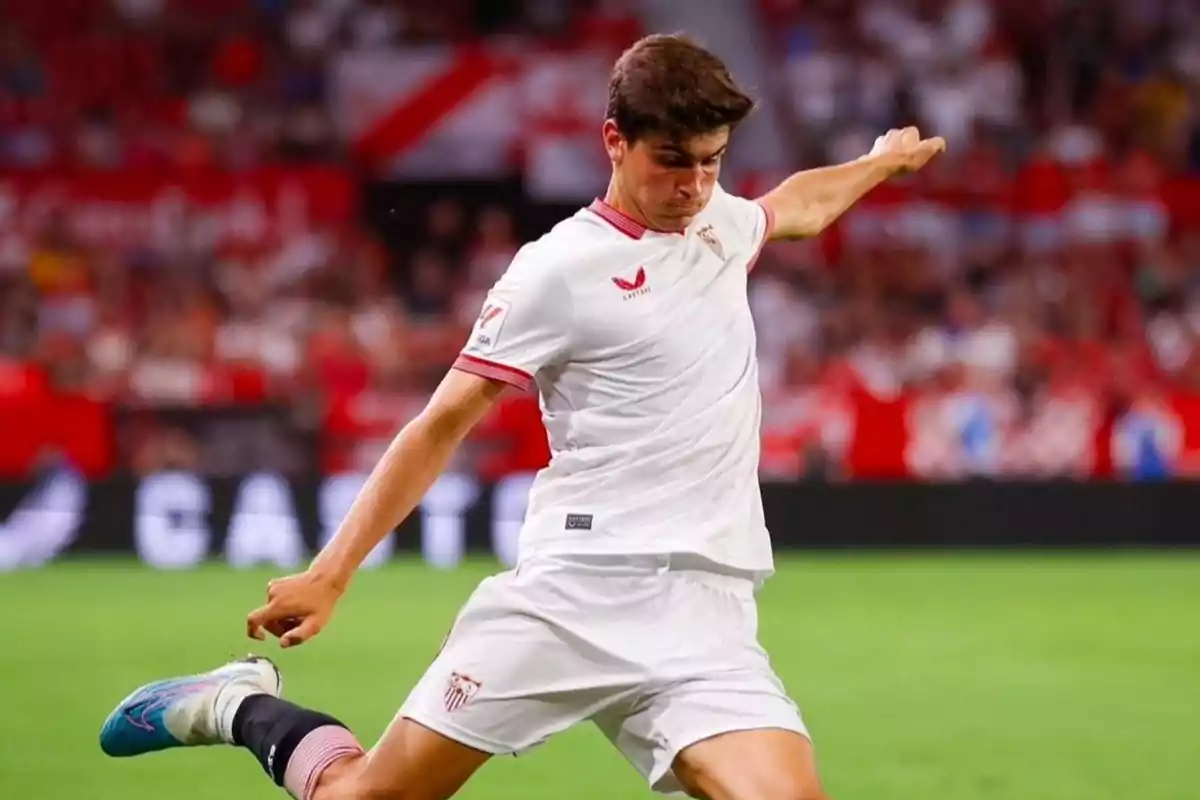 Jugador de fútbol con uniforme blanco pateando el balón en un estadio.