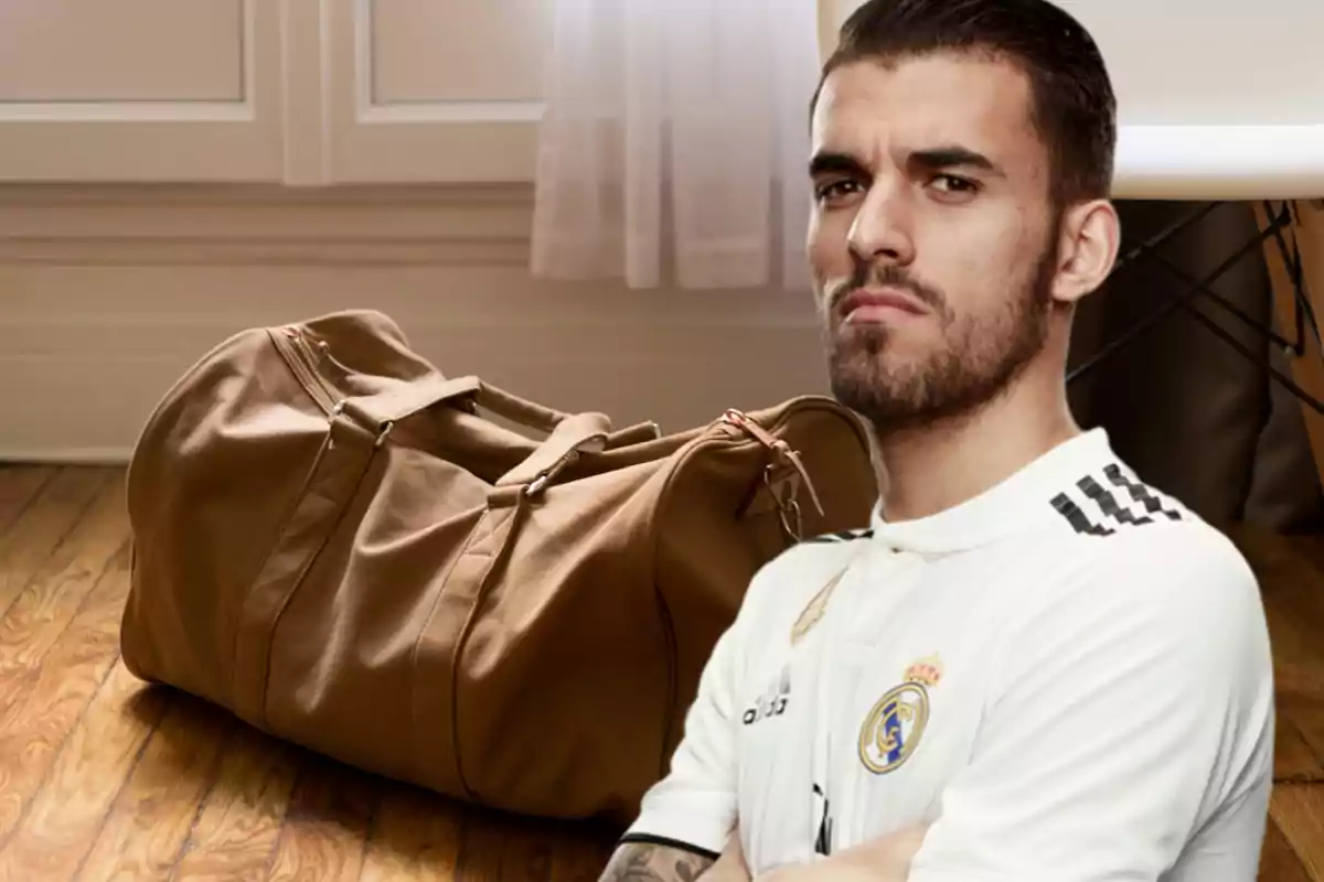 Hombre con camiseta de fútbol blanca junto a una bolsa de viaje marrón en una habitación con suelo de madera.