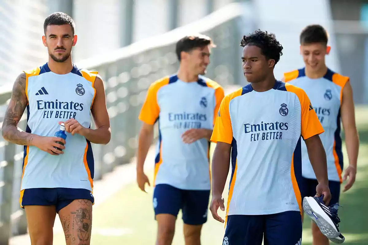 Jugadores de fútbol del Real Madrid caminando en el campo de entrenamiento con uniformes de práctica.