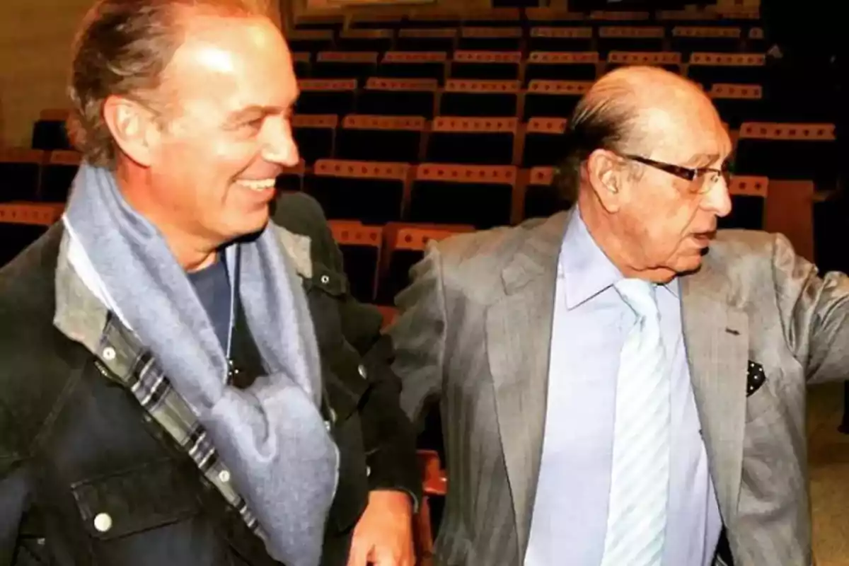 Dos hombres sonrientes conversan en un auditorio vacío.