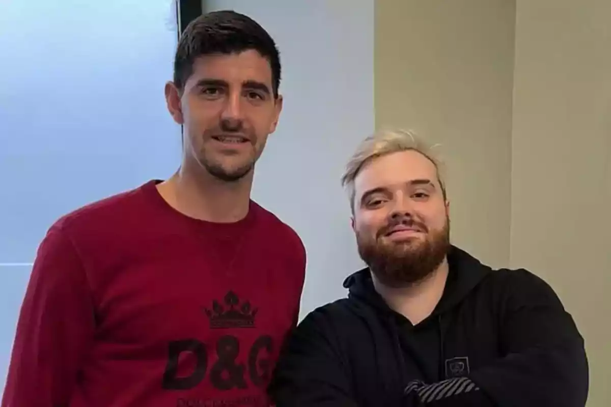 Dos hombres posando juntos, uno con suéter rojo y el otro con sudadera negra.