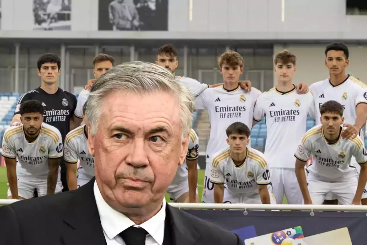 Un entrenador de fútbol con traje negro y corbata está en primer plano, mientras que un grupo de jugadores de fútbol con uniformes blancos del Real Madrid posan detrás de él en un estadio.