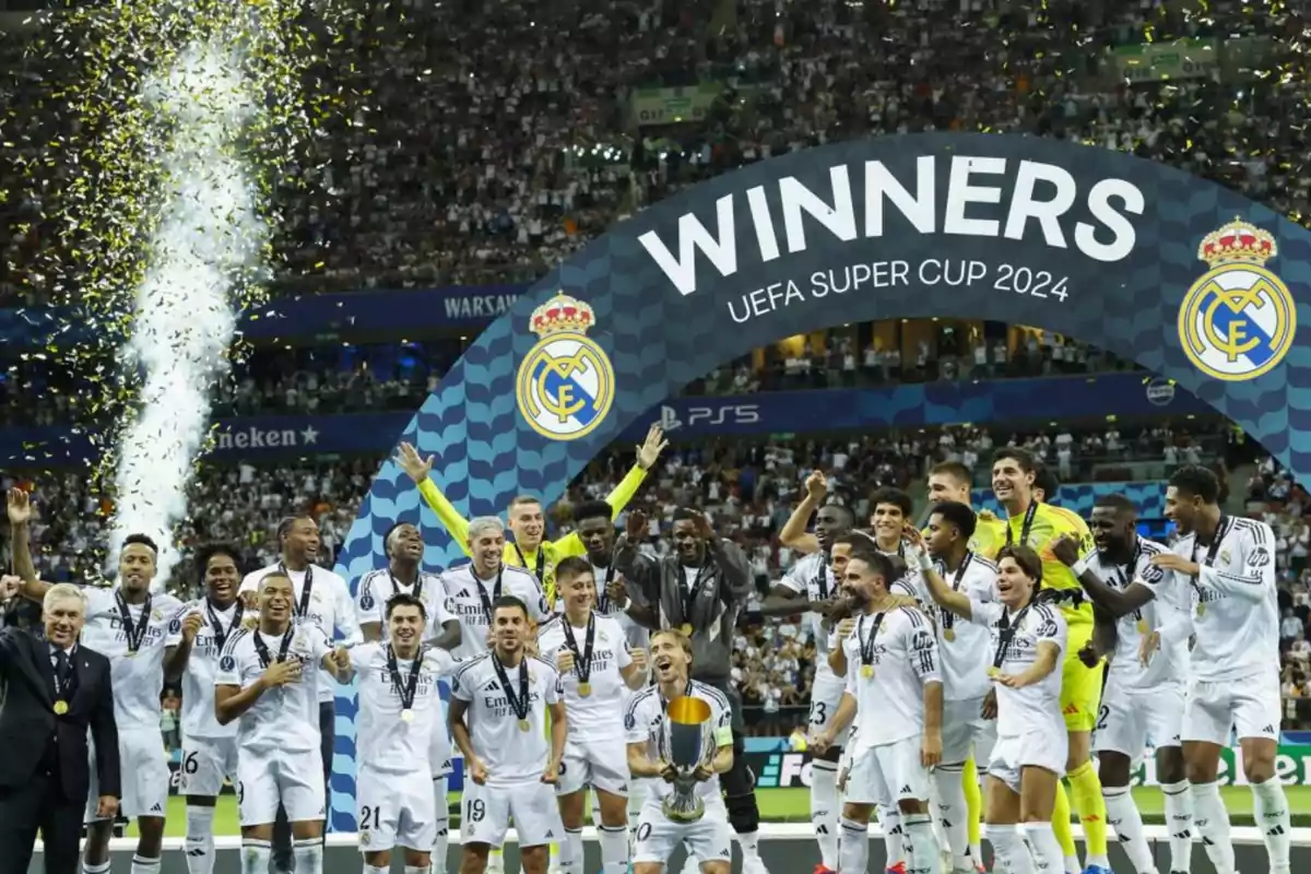 Jugadores del Real Madrid celebrando la victoria en la Supercopa de la UEFA 2024 bajo un arco que dice "Winners" mientras confeti dorado cae alrededor.