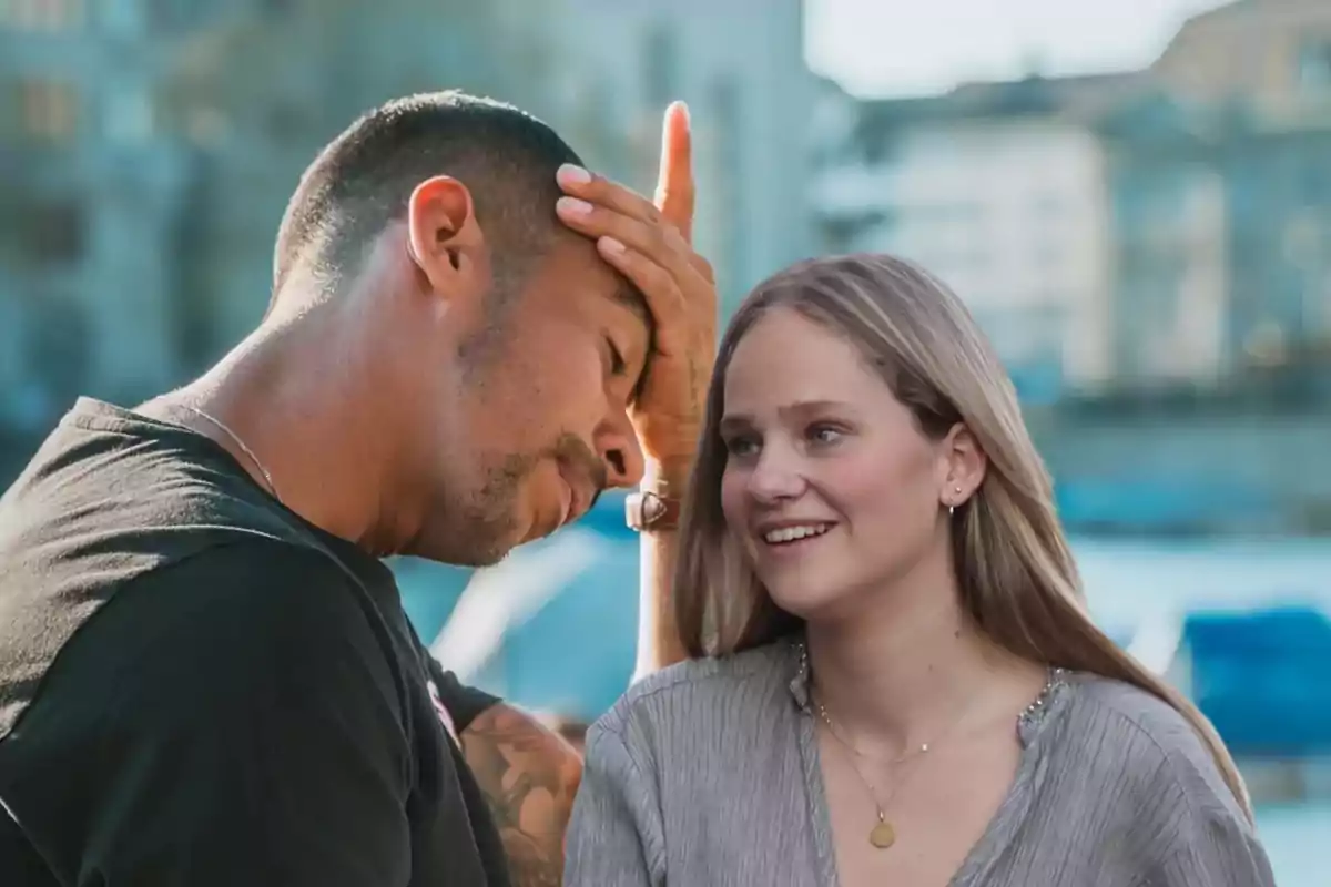 Un hombre con la mano en la frente y una mujer sonriendo mientras conversan al aire libre.