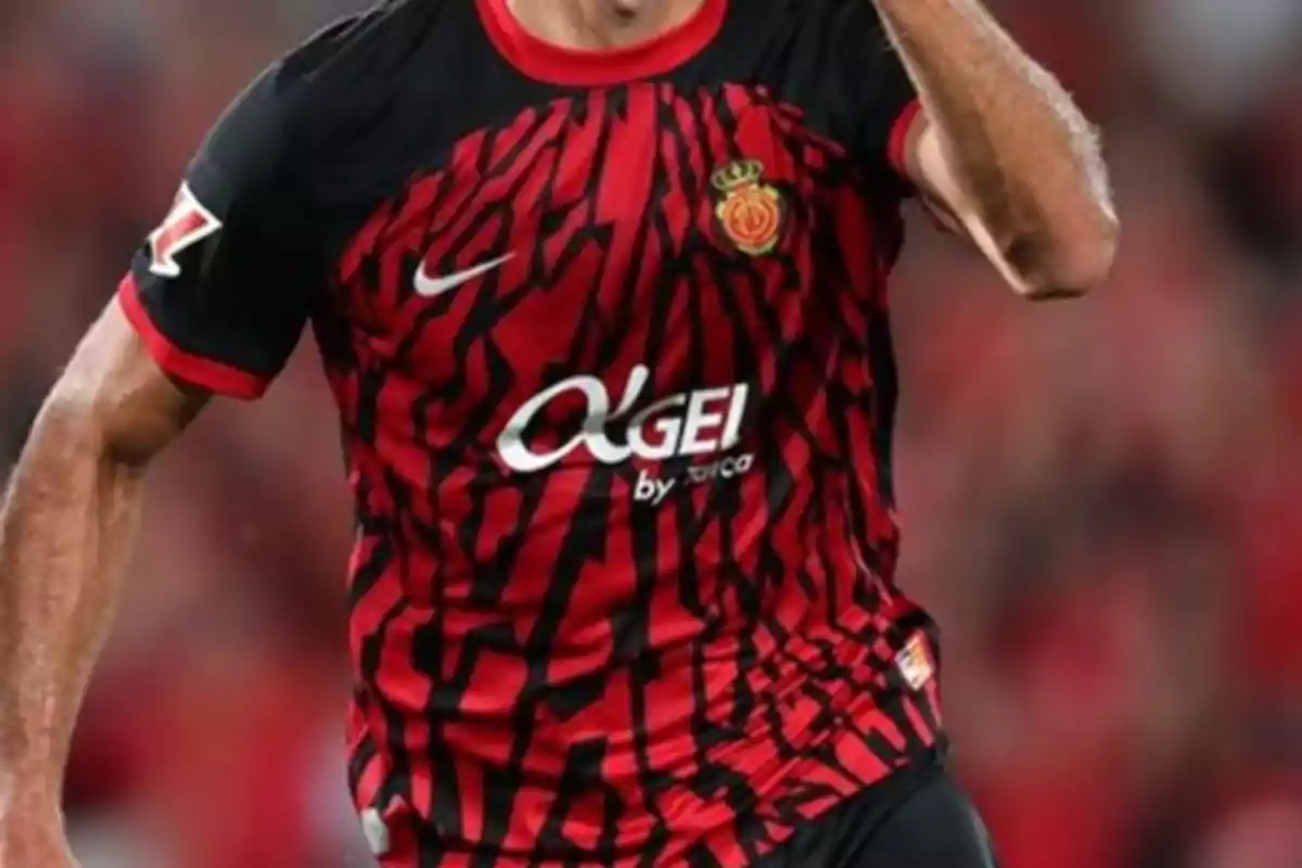 Jugador de fútbol con camiseta roja y negra del RCD Mallorca en el campo de juego.