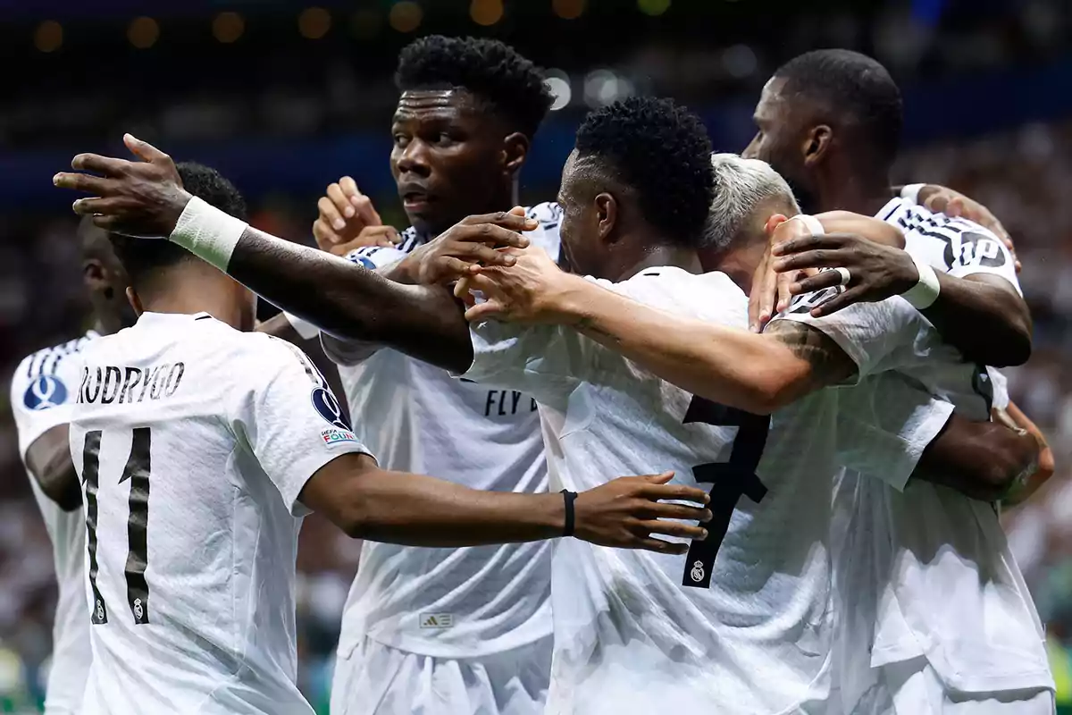 Jugadores de fútbol celebrando un gol en equipo con uniformes blancos.