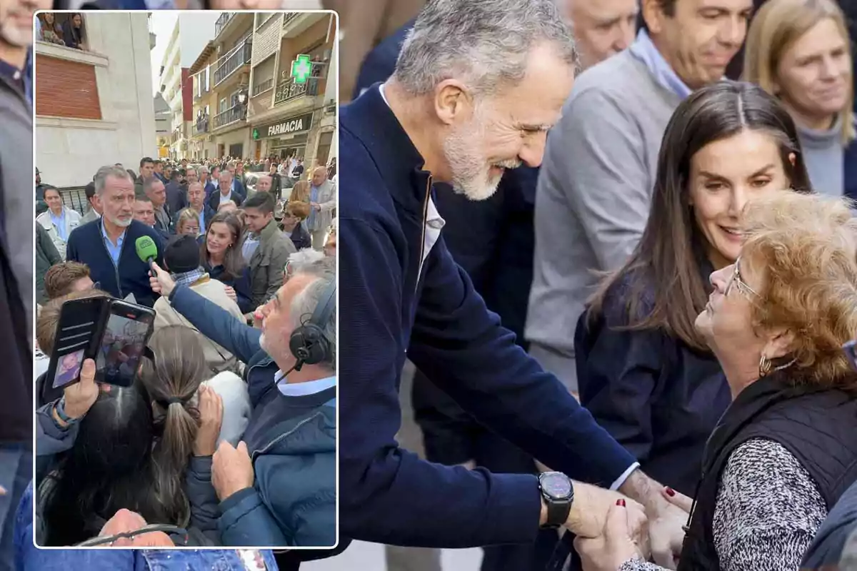 Un hombre de cabello canoso y barba saluda a una mujer mayor en una calle concurrida mientras una multitud los rodea y un reportero sostiene un micrófono cerca.