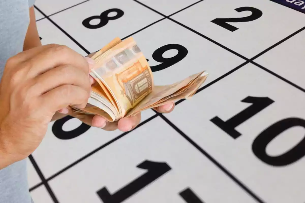 Persona contando billetes de euro frente a un calendario.