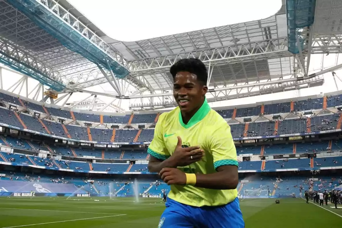 Un jugador de fútbol sonriente con uniforme amarillo y verde corre en un estadio con gradas azules y estructura de techo moderna.