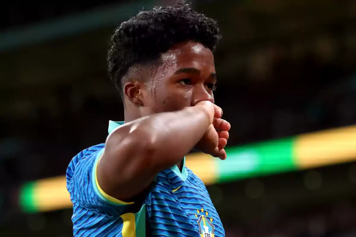 Jugador de fútbol con uniforme azul y amarillo de Brasil, limpiándose el sudor de la cara durante un partido.