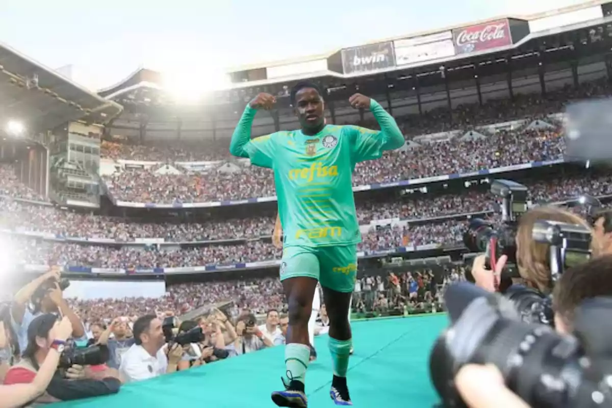 Un futbolista con uniforme verde celebra en un estadio lleno de espectadores mientras los fotógrafos capturan el momento.