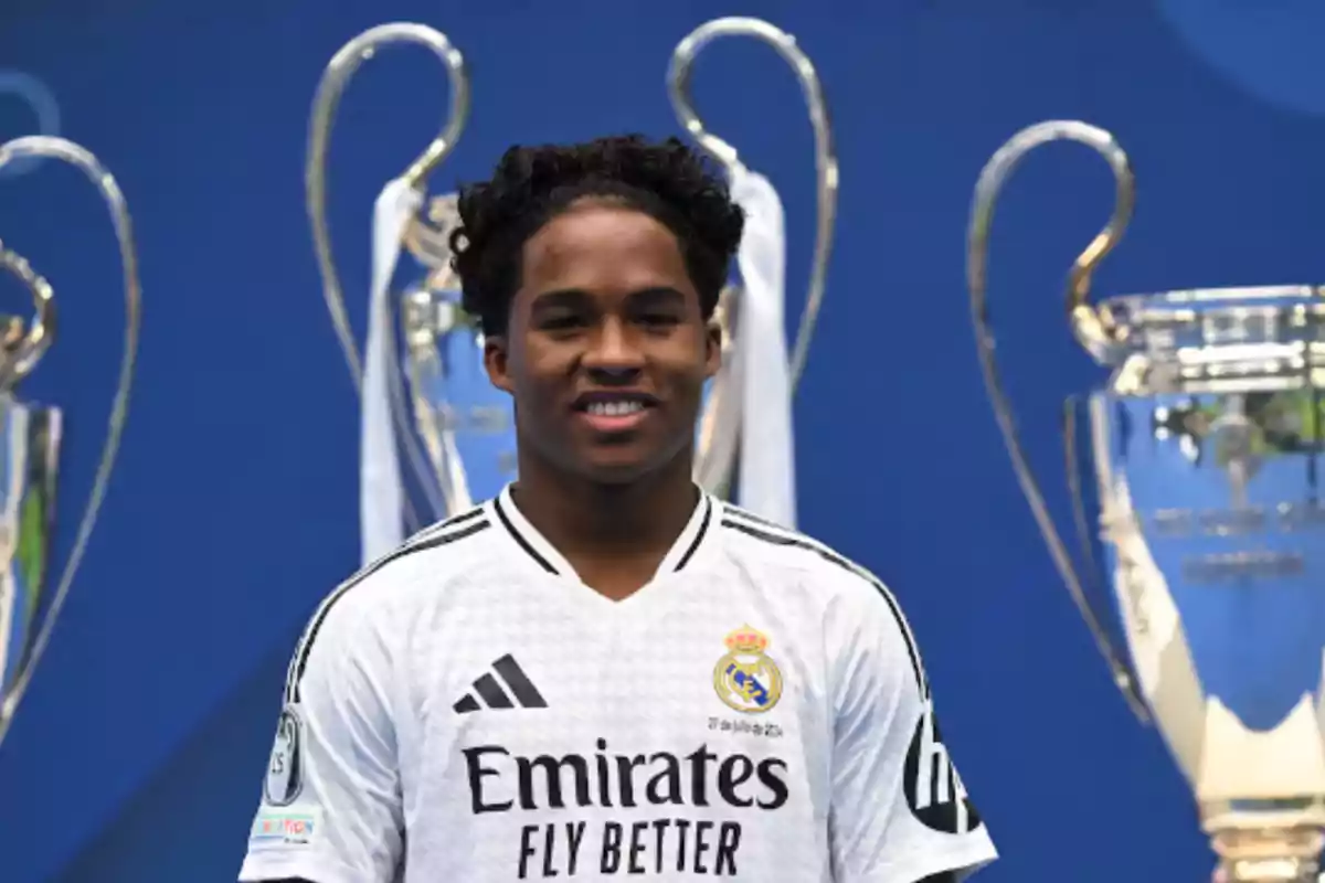 Un jugador de fútbol con la camiseta del Real Madrid posando frente a trofeos.