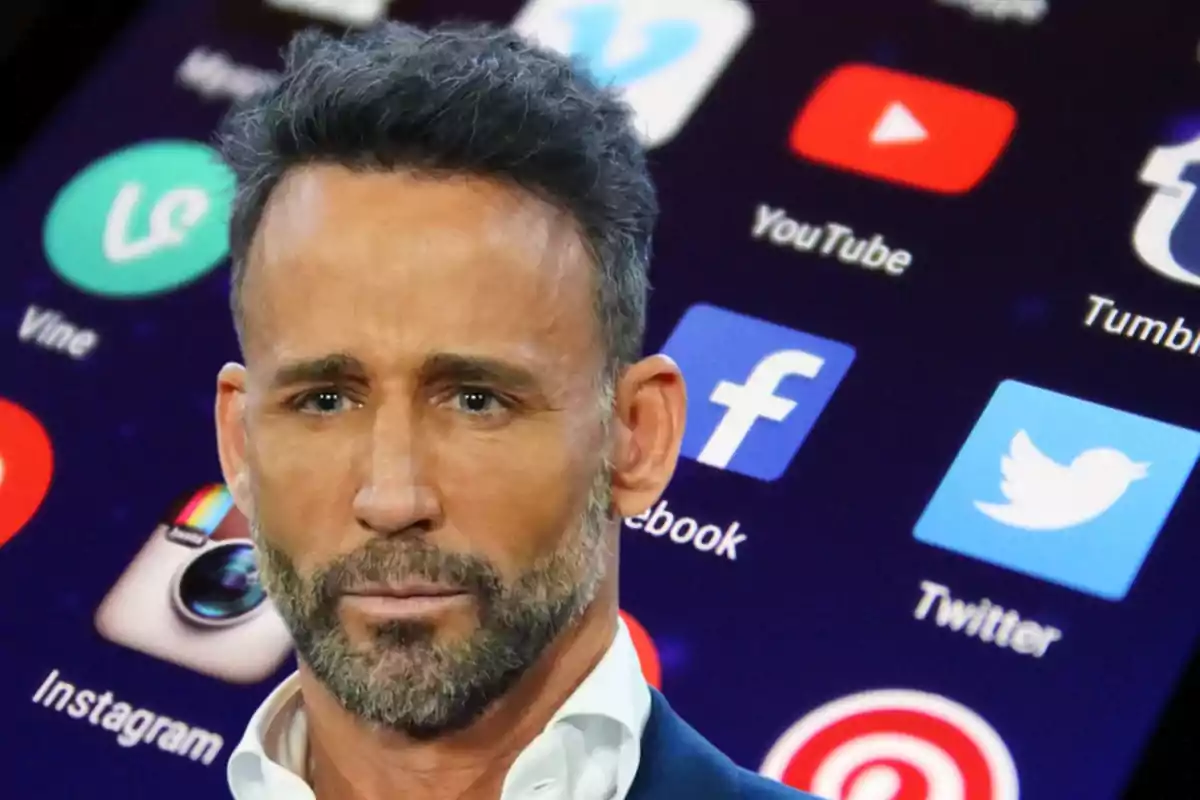 Un hombre con barba y cabello oscuro aparece frente a una pantalla que muestra varios íconos de aplicaciones de redes sociales como Facebook, Twitter, Instagram y YouTube.