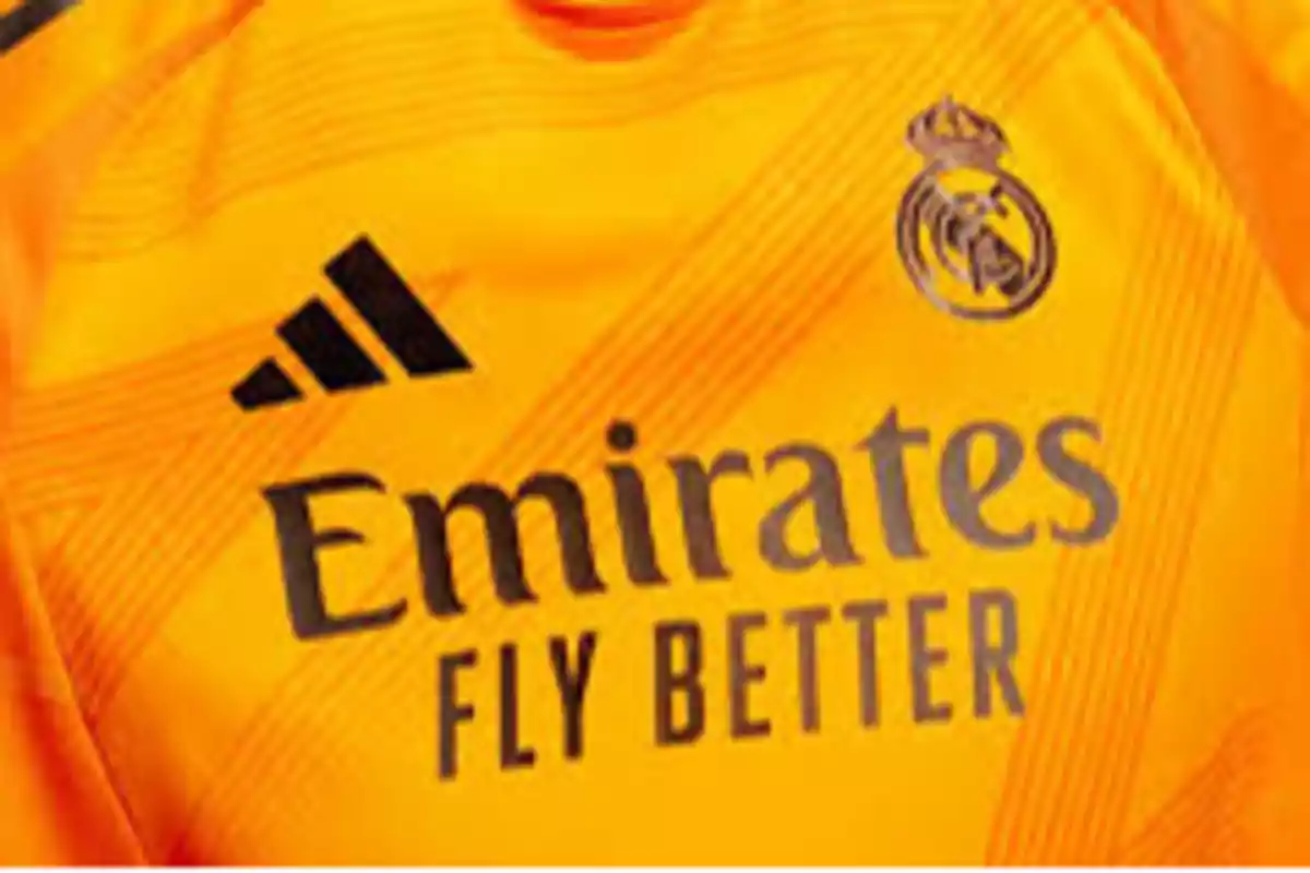 Camiseta de fútbol color naranja con logotipos de Adidas, Emirates y Real Madrid.