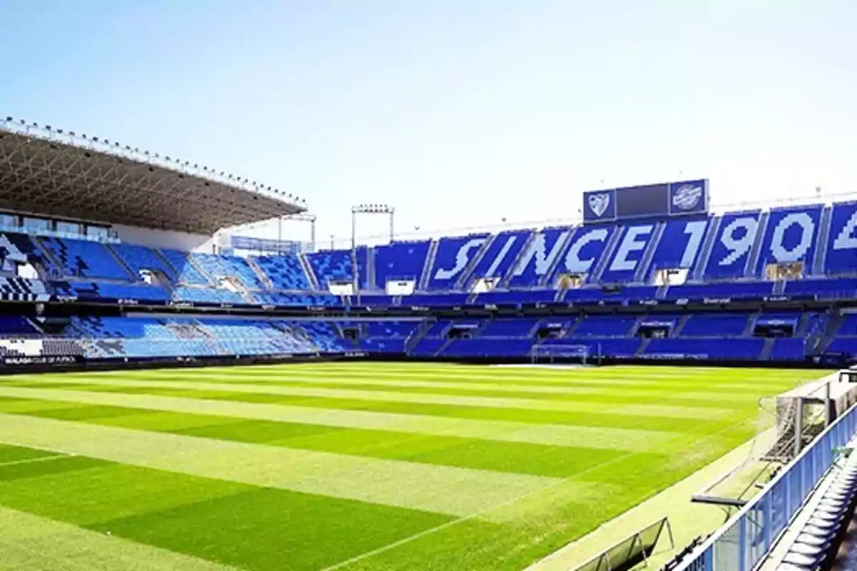 Estadio de fútbol vacío con gradas azules y el texto "SINCE 1904" en los asientos.