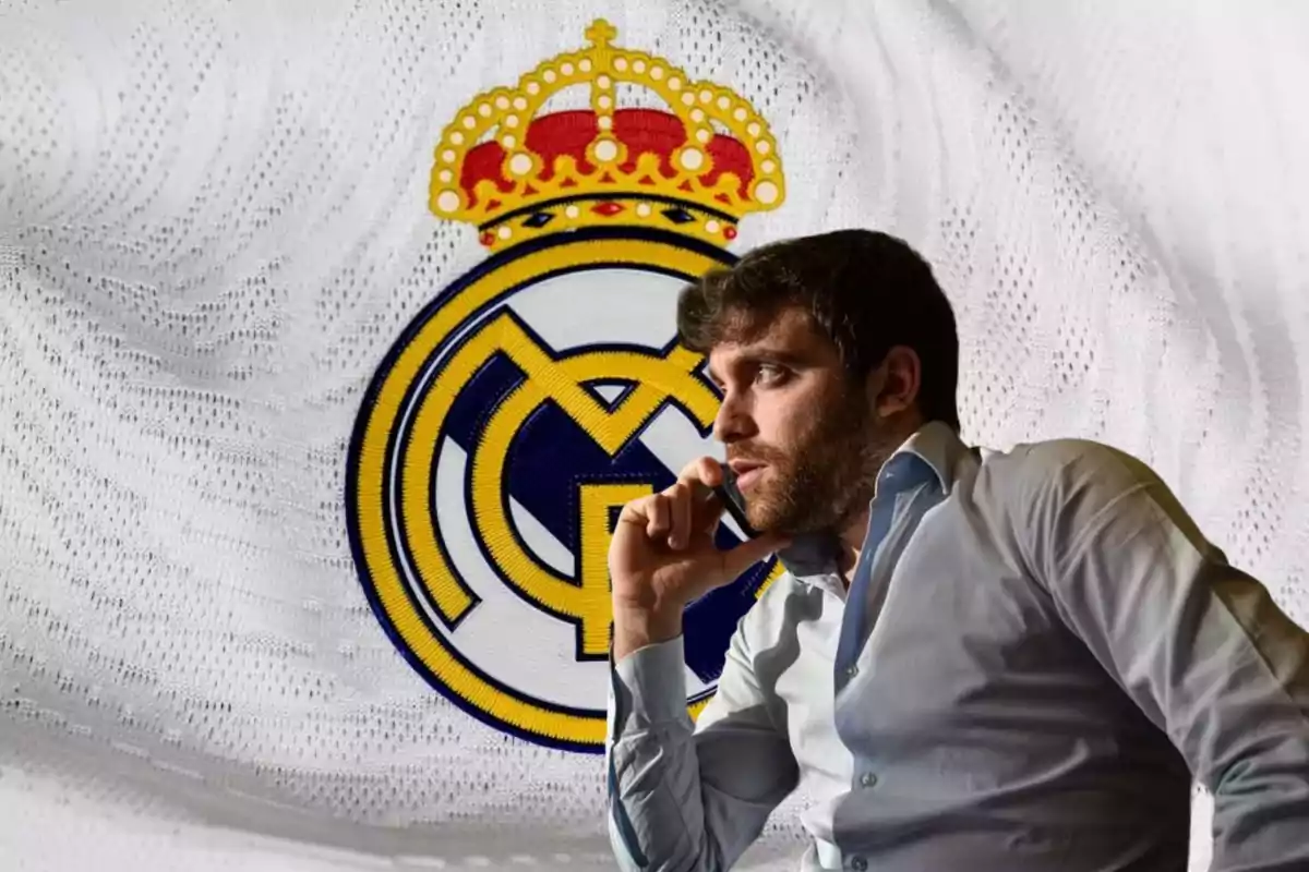 Hombre pensativo con camisa azul claro frente al escudo del Real Madrid.