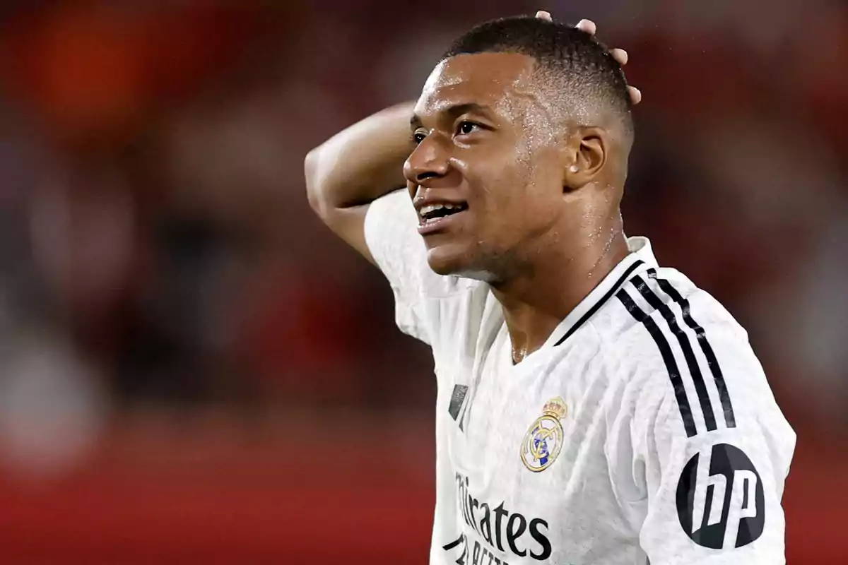 Jugador de fútbol con camiseta blanca del Real Madrid, sudando y tocándose la cabeza.