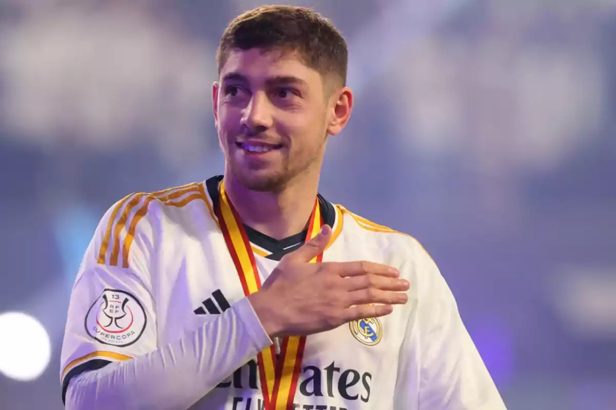 Football player with white uniform and medal around his neck smiles while touching his chest.