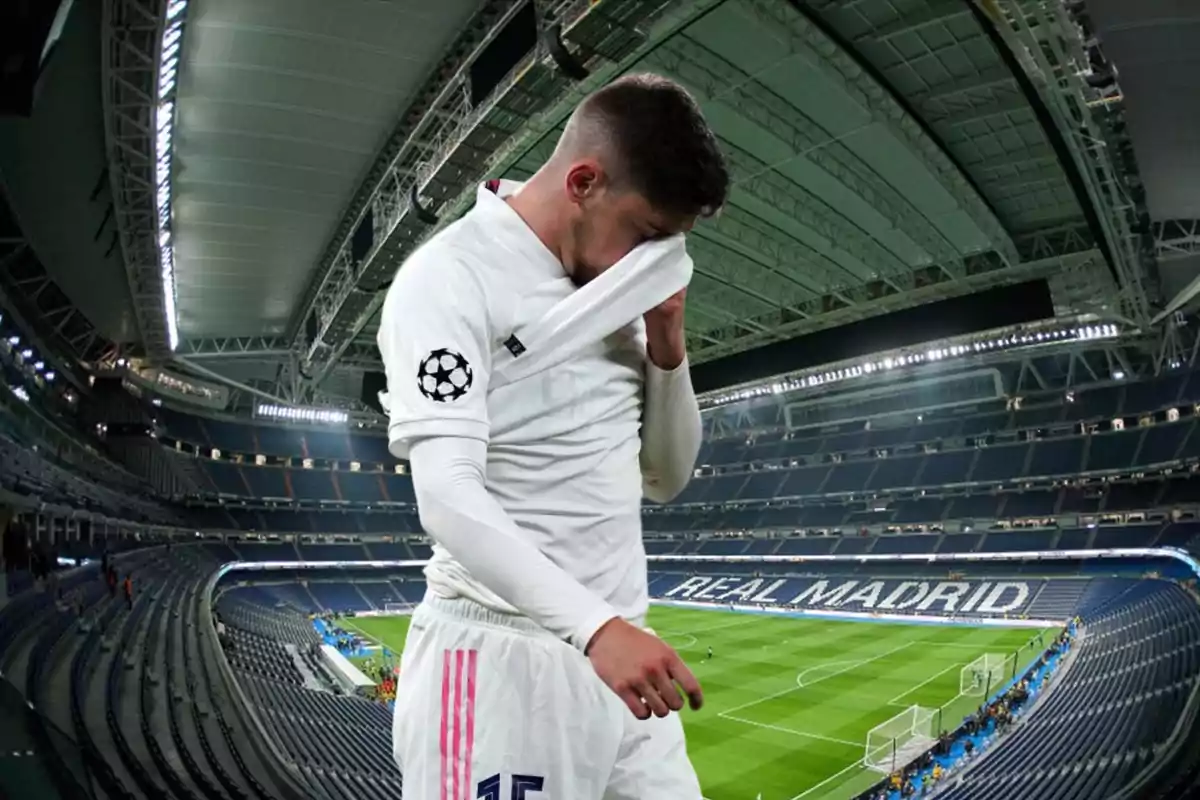 Un jugador de fútbol con uniforme blanco se limpia la cara con su camiseta en un estadio vacío.