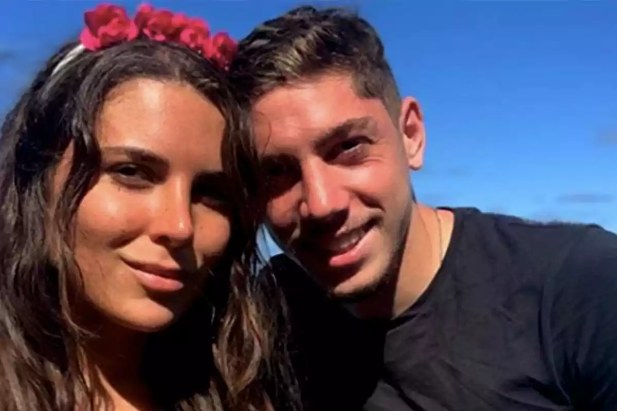 Una pareja sonriente posando al aire libre con un cielo azul de fondo.