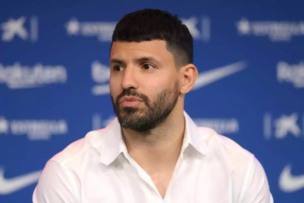 Hombre con barba y cabello corto, vistiendo una camisa blanca, frente a un fondo azul con logotipos.