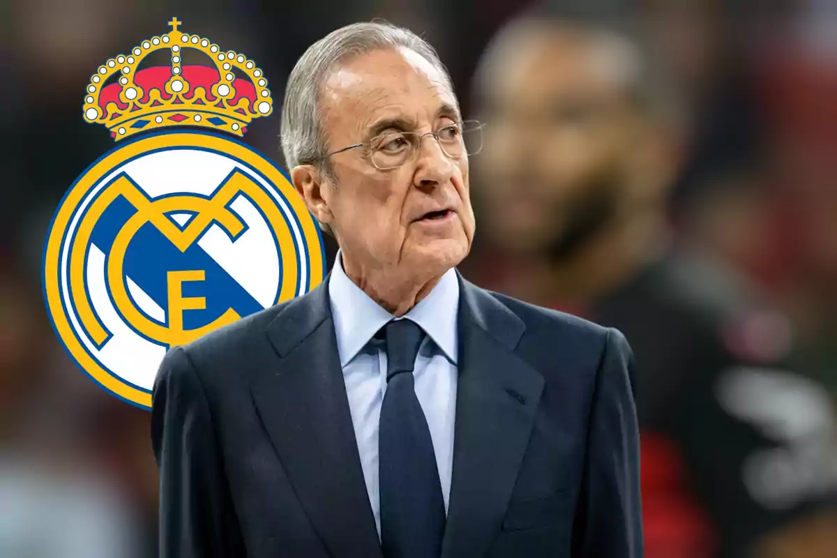 Un hombre con traje y corbata está de pie frente al logo del Real Madrid.