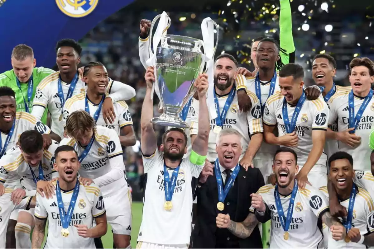 Jugadores de fútbol celebrando con un trofeo grande y medallas alrededor del cuello.