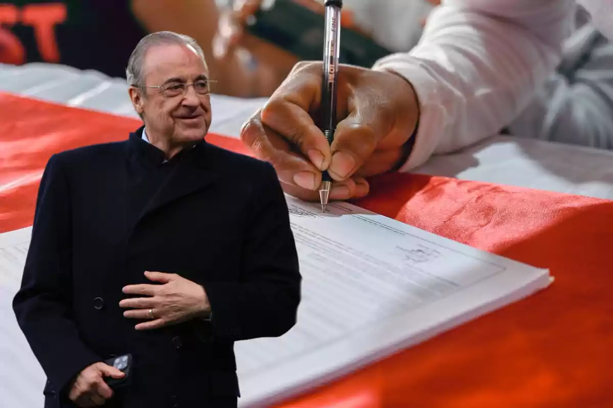 Un hombre de pie con un abrigo oscuro y una mano sosteniendo un control remoto, al fondo una mano firmando un documento sobre una mesa cubierta con un mantel rojo.