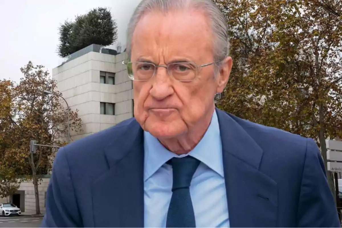 Florentino con gafas y traje azul está de pie frente a un edificio moderno y árboles en otoño.