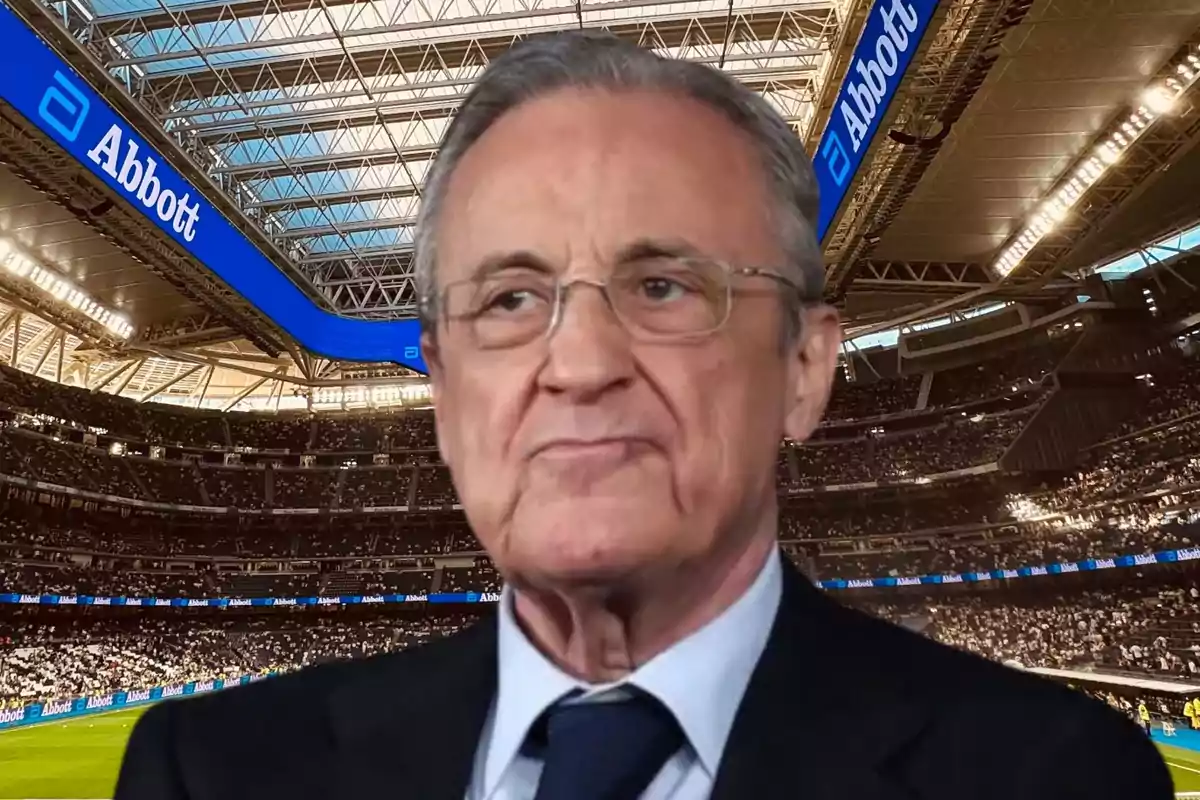 Un hombre con gafas y traje en un estadio lleno de espectadores.