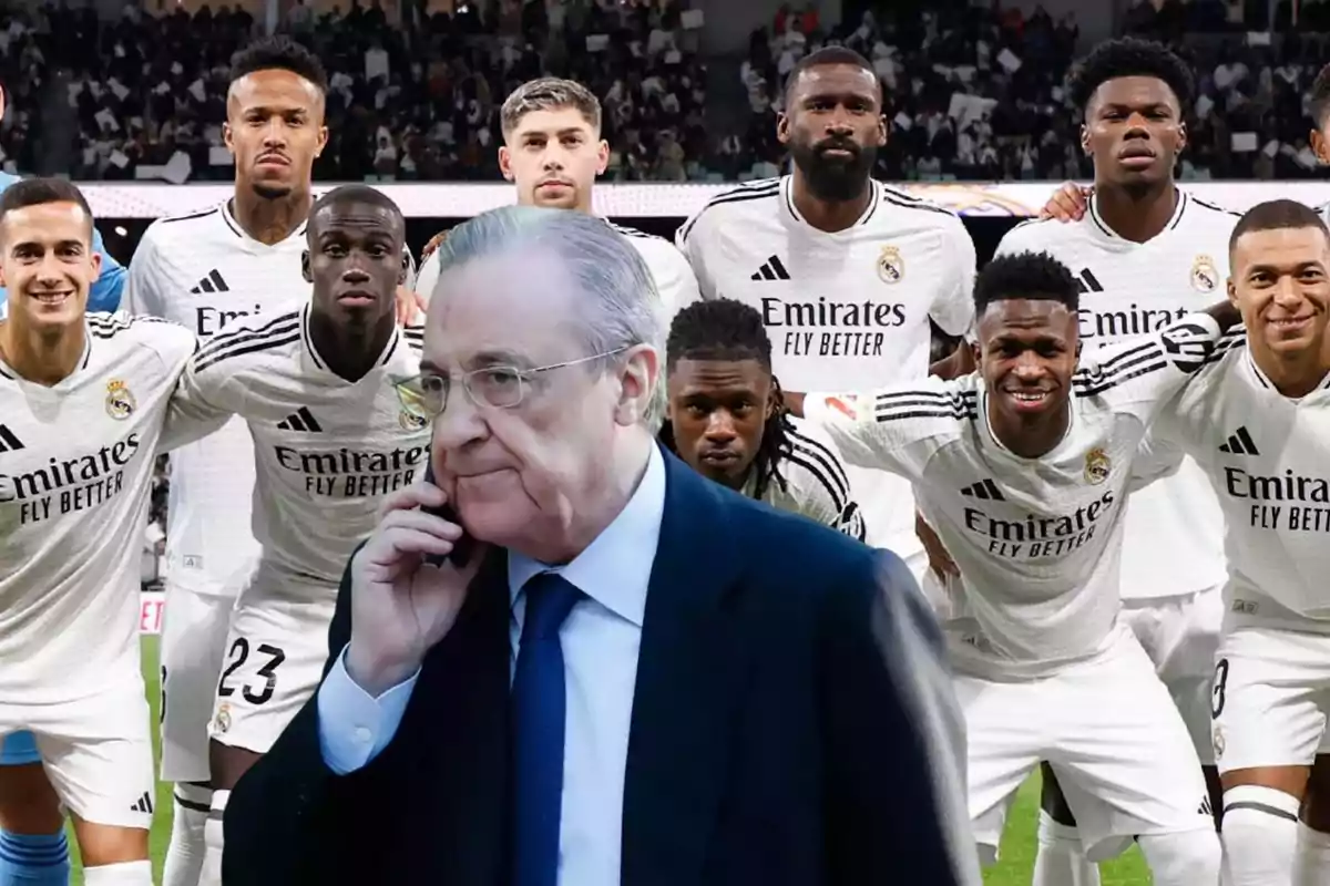 Un grupo de jugadores de fútbol con uniformes blancos posando para una foto en un estadio mientras un hombre de traje habla por teléfono en primer plano.