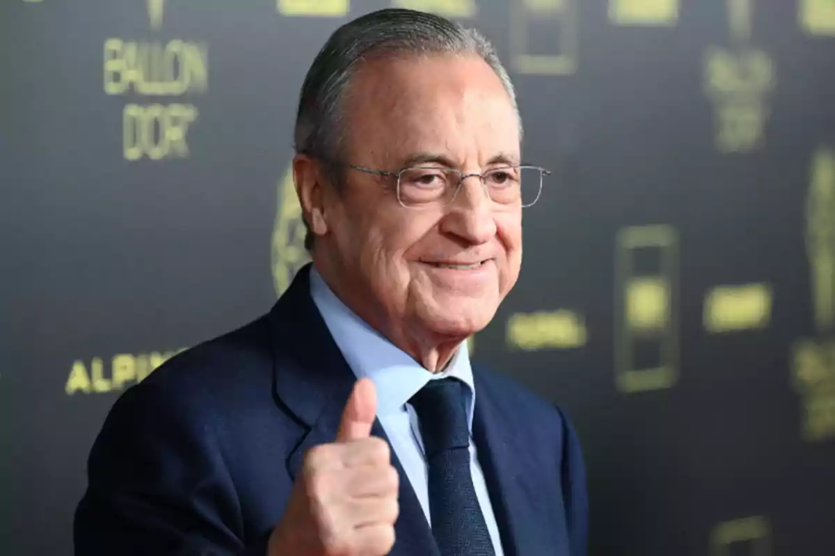 Hombre con gafas y traje azul oscuro haciendo un gesto de aprobación con el pulgar levantado frente a un fondo con el texto "Ballon d'Or".