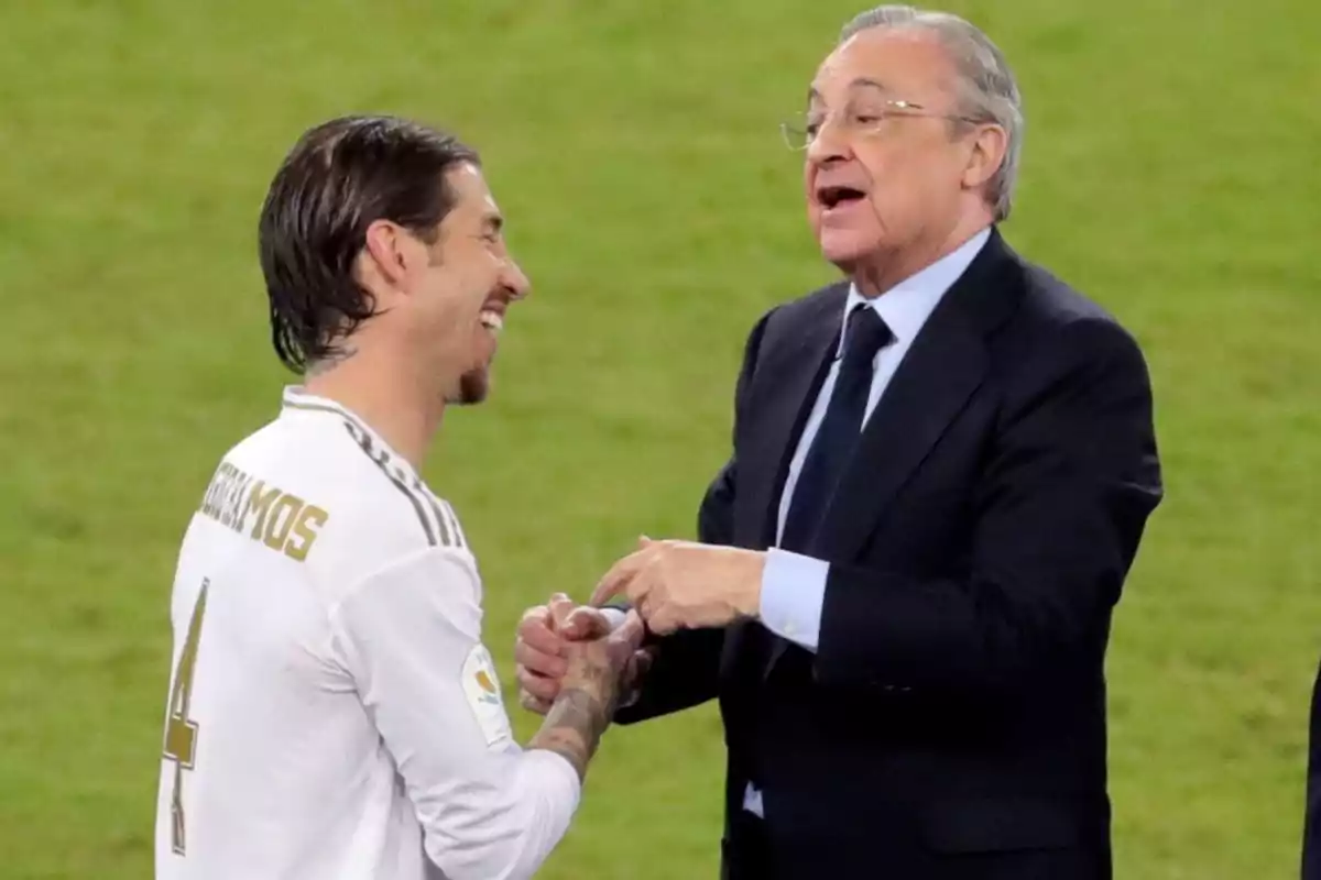 Dos personas conversando y sonriendo en un campo de fútbol.